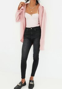 Pink long-sleeve shirt over a white fitted top, paired with high-waisted black skinny jeans and black loafers with gold accents.