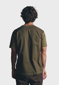 Olijfgroene katoenen t-shirt met een ronde hals en korte mouwen. Glad textuur, ontspannen fit en een klein vierkant label aan de achterkant van de hals.