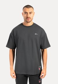 Camiseta de manga corta de color gris oscuro, hecha de tela suave. Presenta un cuello redondo, un logo en el pecho y etiquetas en el dobladillo inferior. Ajuste simple y relajado.
