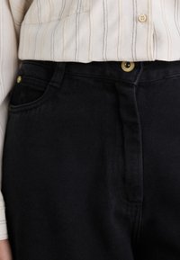 Black denim jeans with a smooth texture, featuring a classic five-pocket design and a gold button closure at the waist.