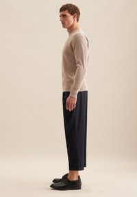 Beige geripptes Sweatshirt, marineblaue maßgeschneiderte Hose und schwarze Schuhe. Einfaches Design, taillierte Silhouette, glatte Textur und subtile Farbkontraste.