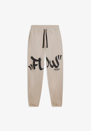 Pantalon de survêtement beige en tissu doux avec une taille à cordon de serrage, arborant un grand graphique noir "FLOW" et le texte "FREDDY" sur la jambe gauche.