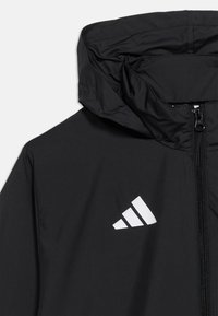 Μαύρο μπουφάν με κουκούλα, εμπρός φερμουάρ και λευκό τρίγωνο λογότυπο της Adidas στο αριστερό στήθος.