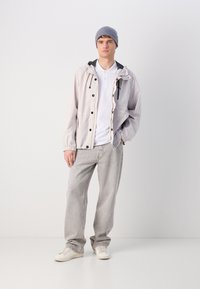 Light gray, water-resistant jacket with a hood, black accents, and snap buttons. Paired with white shirt, gray pants, and white sneakers.