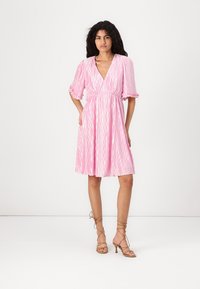 Rosa midi-klänning med V-ringning, korta volangärmar och texturerat vågigt mönster. Stylar med bruna klackar med remmar.