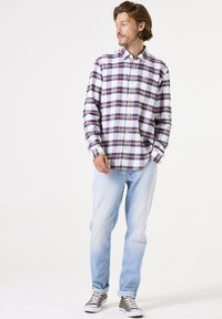 Geruite shirt met blauwe, rode en witte patronen, met knopen. Lichtdenim jeans en grijze sneakers maken de casual look compleet.