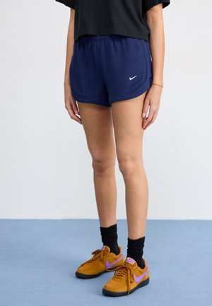 Shorts de sport à côtes bleu marine avec une taille élastique et un logo blanc, associés à des baskets marron et violettes et des chaussettes noires mi-mollet.