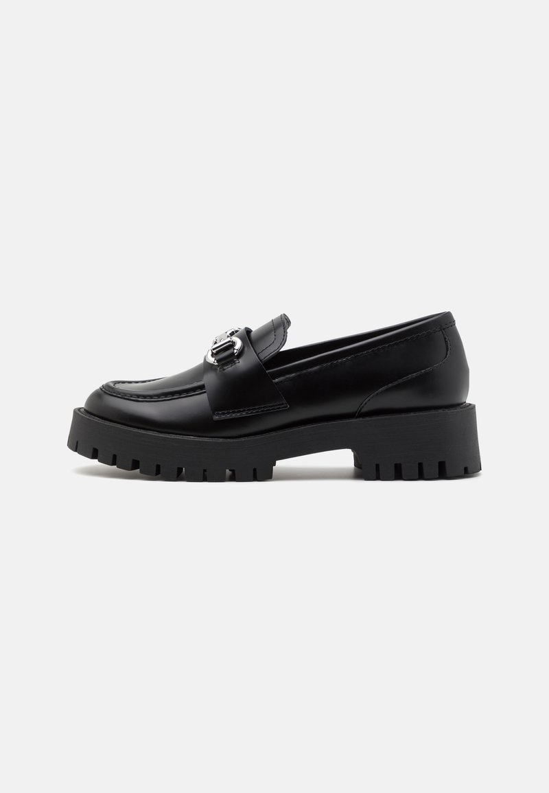 Mocassin en cuir noir avec une semelle épaisse noire, doté d'une boucle argentée proéminente sur le cou-de-pied et de détails de couture visibles.