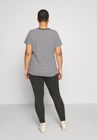 Randig t-shirt i svart och vitt, kort ärm, avslappnad passform; kombinerad med mörkgrå leggings och ljusa sneakers.