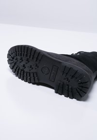 Schwarzlederne Stiefelsohle mit tiefen Profilmustern, strapazierfähigem Gummimaterial und einem eingestempelten Timberland-Logo in der Mitte.