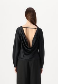 Blusa in satin nero con schiena drappeggiata, maniche lunghe e scollatura a V profonda. Presenta una sottile tracolla sul retro. Texture liscia, design elegante.