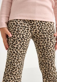 Leopard print pants in beige with black spots, cotton material, slightly fitted design, worn with a light pink ribbed long-sleeve top.