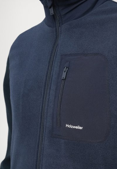 Jachetă fleece bleumarin cu buzunar cu fermoar pe piept cu logo, guler înalt și mâneci texturate pentru un plus de contrast și interes.