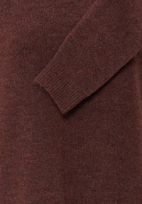 Gros plan d’un pull en maille marron avec une manche longue posée sur le devant, mettant en valeur le tissu doux et texturé.