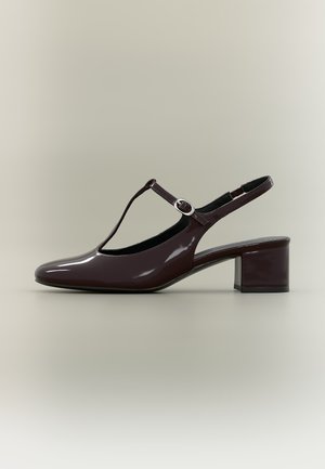 Σκούρο καφέ παπούτσι τύπου slingback από λουστρίνι, με λουρί T, χοντρό τακούνι και ασημένια αγκράφα σε ουδέτερο φόντο.