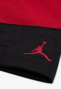 Röd och svart tyg med en slät yta; har en Jumpman-logga i rött på den svarta delen. Designen inkluderar kontrasterande färger.