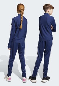 Námornícke športové teplákové súpravy pre deti, s bielymi bočnými pruhmi, textúrovaným materiálom, zipsom na golieri a priliehavými nohavicami. Topánky v kontrastných štýloch.