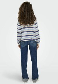 Stickad tröja i blå och krämfärgad zigzag-mönster, i kombination med utsvängda denimjeans. Tröjan har en lös passform och ribbade muddar.