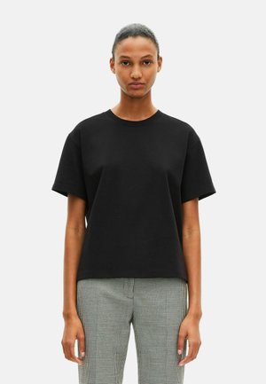 T-shirt en coton noir avec un col ras du cou, des manches courtes et une coupe décontractée, associé à un pantalon à carreaux. Design minimaliste, sans motifs.
