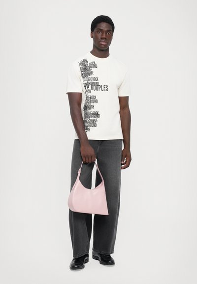 Λευκό γραφικό μπλουζάκι με μαύρο κείμενο, σε συνδυασμό με σκούρες γκρι φαρδιές τζιν. Μια ανοιχτή ροζ δερμάτινη τσάντα κρατείται στο δεξί χέρι.