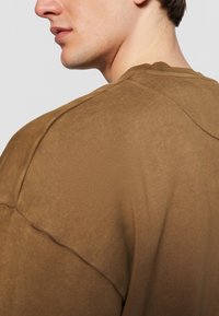 Brun strikket t-shirt med afslappet pasform og synlige sømdetaljer, rund crew neckline og blødt, tekstureret stof.