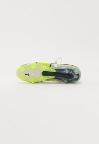 Botas de fútbol con un diseño predominantemente plateado y amarillo, que presentan una parte superior texturizada, acentos negros en contraste y una suela de goma moldeada.