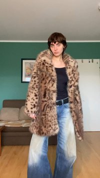 Bruine jas van nepbont met een luipaardprint, lange mouwen en een zachte textuur, gecombineerd met vervaagde brede blauwe jeans.