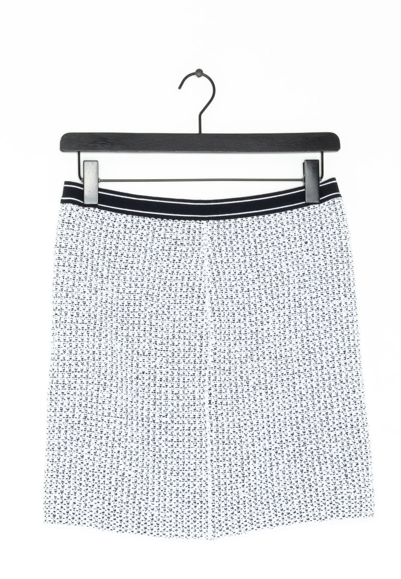 Jupe texturée blanche et noire avec une ceinture rayée noire et blanche suspendue à un cintre noir sur fond blanc.