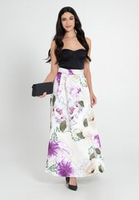 Top nero senza spalline e lungo gonna bianca con motivi floreali viola e verdi. Una pochette nera e tacchi alti completano il look.