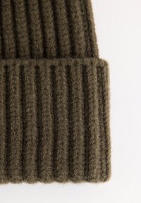 Gros plan sur un bonnet en tricot côtelé plié de couleur vert olive foncé sur un fond blanc.