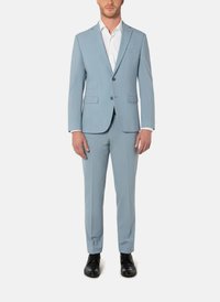 Vaaleansininen puku klassisella leikkauksella, jossa yksirivinen bleiseri, läppäkaulus ja mustat napit. Yhdistetty vastaaviin housuihin.