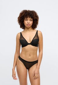 Ensemble de lingerie noire comprenant un soutien-gorge en maille transparente avec un design en V et un string coordonné en maille transparente. Tissu lisse avec un minimum de matériel.