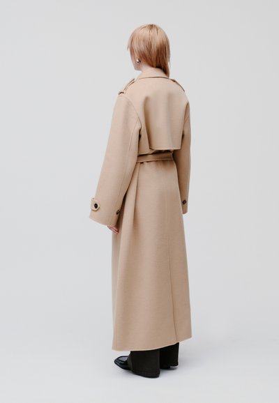 Cappotto oversized beige in lana con retro accorciato, ampie maniche e cintura. Presenta una silhouette pulita e un design minimalista.
