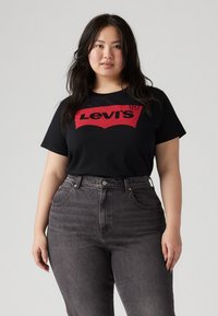 Tricou negru cu un logo mare roșu Levi's, asortat cu blugi gri închis, cu talie înaltă. Materialul pare neted; croială lejeră, cu mâneci scurte.