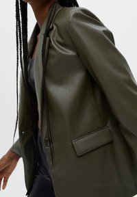 Blazer en simili cuir vert olive avec un bouton unique, revers crantés et poche poitrine, doté d'une texture lisse et d'une coupe structurée.