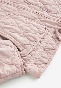 Tissu rose matelassé, avec une texture douce. Présente un motif cousu subtil et une finition satinée. Comprend des poches et une bordure.