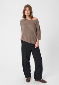 Overdrevet brun strikket sweater med bred Halsudskæring, parret med sorte højtaljede bukser og brune ruskindssko. Glat tekstur.