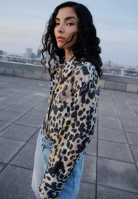 Camicia in seta con stampa leopardata e chiusura a bottoni, dotata di maniche lunghe e vestibilità morbida, abbinata a jeans in denim blu chiaro.
