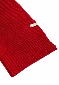 Czerwony dziany szalik o prążkowanej fakturze z naszywką z haftowanym logo. Krawędzie są gładko wykończone, co tworzy schludny wygląd.