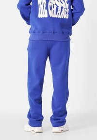 Blauwe sweatshirt en bijpassende trainingsbroek van zacht materiaal. De sweatshirt heeft witte tekst; de broek heeft een elastische tailleband en boorden.