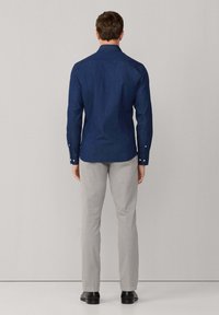 Granatowa, długosleeve koszula z guzikami, z kołnierzykiem i guzikami na mankietach, w połączeniu z jasnoszarymi spodniami i czarnymi butami, przedstawiona z tyłu.