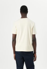 Cream-colored, short-sleeved t-shirt in soft cotton, features a round neck and a relaxed fit, viewed from the back.