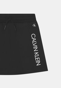 Czarne szorty z miękkiego materiału ze sznurkiem w talii. Posiadają białe logo "CALVIN KLEIN" nadrukowane pionowo po lewej stronie.
