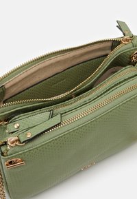 Borsa verde dalla texture con cerniere dorate, multiple tasche e foderatura interna liscia. Caratterizzata da un design elegante e dettagli con cerniera.