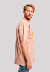 Pink cotton t-shirt with short sleeves, featuring a graphic design on the front. The fit is relaxed, paired with light blue jeans.
