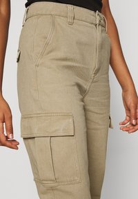 Khaki cargo kalhoty s bočními kapsami, vyrobené z texturované tkaniny, s vysokým pasem a viditelnými švy.