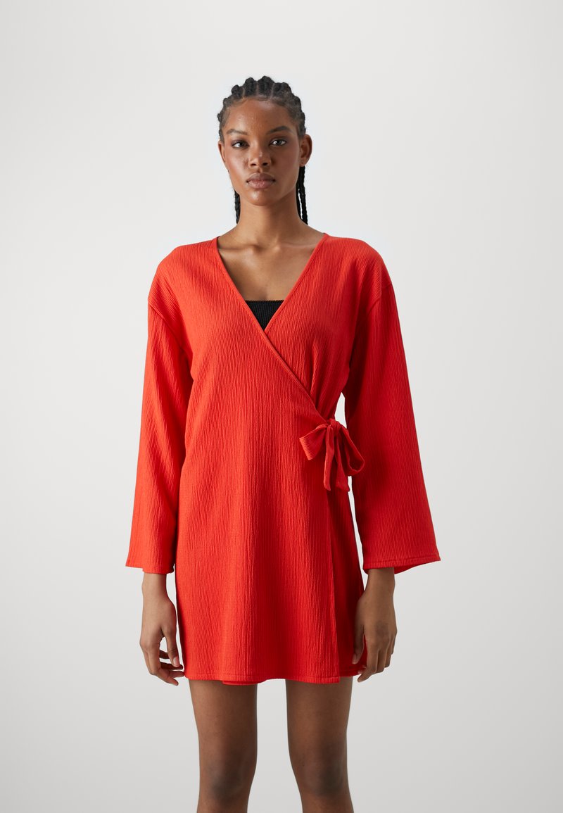 Vestido rojo ajustado con mangas largas, tejido texturizado, escote en forma de V y un detalle de lazada en la cintura. Presenta un dobladillo recto y un diseño sencillo.