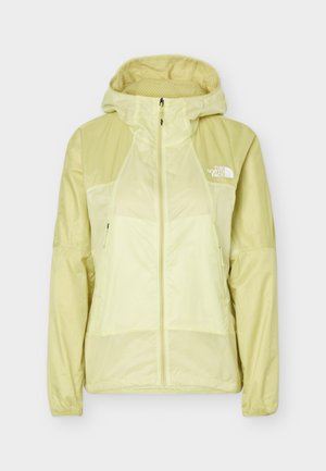Veste coupe-vent jaune clair à fermeture éclair intégrale avec capuche, manches longues, deux poches zippées à l'avant et logo The North Face sur le côté gauche de la poitrine.