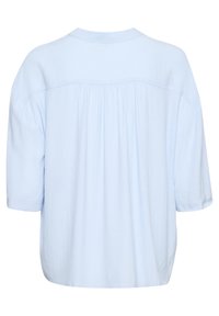 Blusa azzurro chiaro a maniche corte con una texture morbida, scollo rotondo e dettaglio arricciato sul retro. Vestibilità ampia con taglio dritto e senza hardware visibile.