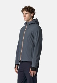 Szara wodoodporna kurtka z kapturem, z zamkiem błyskawicznym z kolorowym suwakiem oraz elastycznymi mankietami, zaprojektowana do aktywności na świeżym powietrzu.